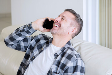 Happy young man making a phone call at home