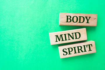body, mind and spirit words on wooden blocks on green background.
