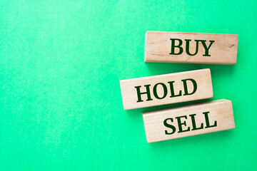 buy, hold, sell words on wooden blocks on green background.