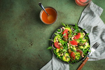 Healthy vegan salad with arugula, avocado, juicy grapefruit, cashews and dressing with olive oil,...