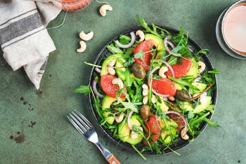 Healthy vegan salad with arugula, avocado, juicy grapefruit, cashews and dressing with olive oil, honey and wine vinegar. Green rustic kitchen table, top view, copy space