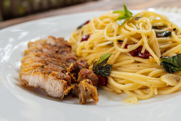 Thai-style stir-fried spaghetti with dried chilli sauce and hot, tender and delicious pork cutlets are served in a white plate on a wooden table, resulting in a spicy spaghetti and fragrant pork cutle