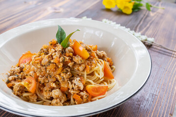 Spaghetti stir-fried with tomato sauce and minced chicken in hot Thai style. Tender and delicious served in a white plate placed on a wooden table, resulting in a delicious spaghetti from the sauce.