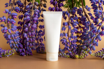Mockup of white squeeze bottle plastic tube for branding of medicine or cosmetics - cream, gel, skincare. Cosmetic bottle container and lupine flowers on golden background.