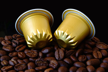 Closeup of isolated gold color aluminum coffee capsules with fresh brown coffee beans. convenient way of coffee brewing. abstract macro view. black background. food and drink theme. macro view.