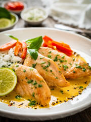 Fried chicken breasts in curry sauce with white rice on wooden table
