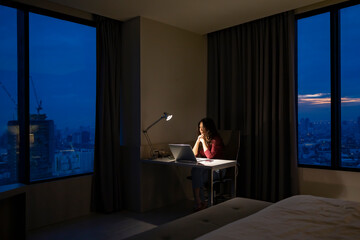 Feeling exhausted. Beautiful asian woman working on a laptop sitting in her bedroom near window at...