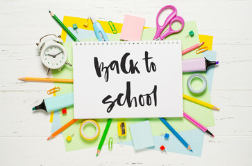 Children's accessories for study, creativity and office supplies on a white wooden background. Handwritten inscription Back to school on a white notebook.