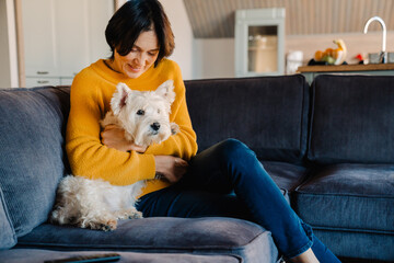 White mature woman hugging her dog while sitting on couch