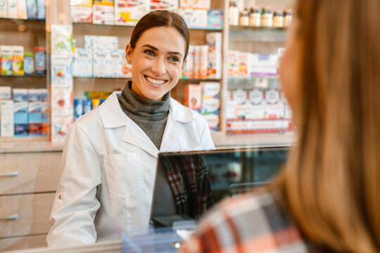 White apothecary wearing lab coat working with customer in pharmacy