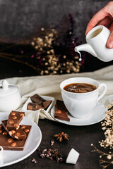 Coffee in a white cup with chocolate flowers hand pours milk from milkweed freeze drops black background
