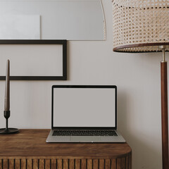 Laptop computer with blank screen on table with candles, floor lamp. Aesthetic boho styled home...