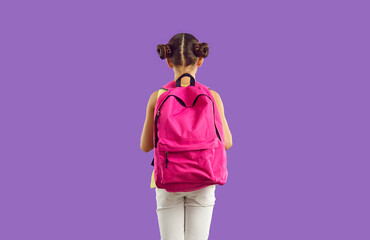 Back to school. New roomy pink school backpack on back of little girl, isolated on purple background. Schoolgirl with hairstyle with two bundles demonstrates new collection of school bags. Advertising
