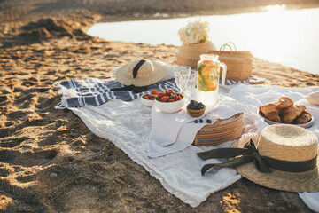 Beautiful picnic with fresh fruits, lemonade and croissants on the beach at sunset.