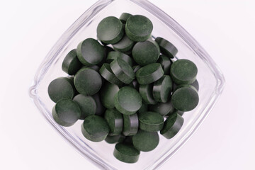 Green spirulina tablets in a glass bowl.Close-up.