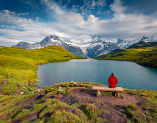 Tourist siting on bench on the shore of Bachalpsee lake with Schreckhorn peak on background....