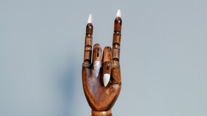 A wooden mannequin hand with gel nails doing a rock n roll hand gesture, with a clean background
