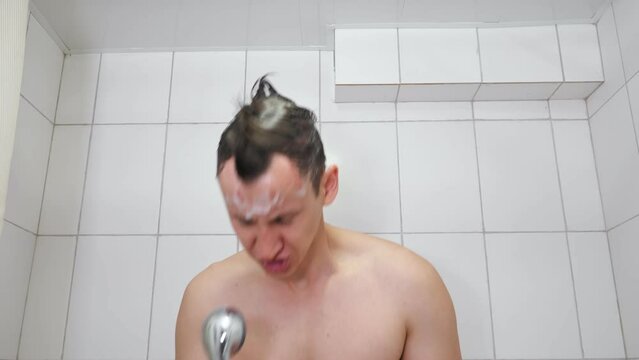 Man with bare torso takes shower dancing and singing. Strong guy moves and sings rock using shower head as microphone in bathroom
