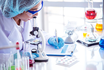 Fototapeta premium Asian Woman scientist hand write note research in medical lab look at science microscope medical test. Researcher biology chemistry. Asian Female technician laboratory using microscope blood test