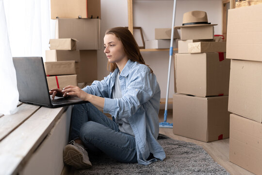 Young girl sitting on the floor using laptop computer wireless internet, moving to a new house, moving day