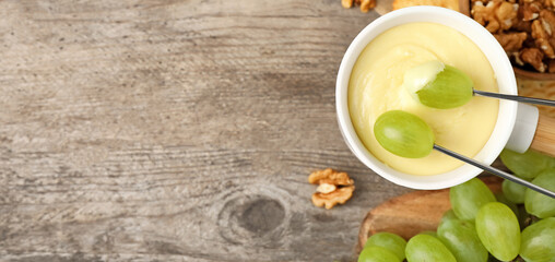 Dipping grapes into fondue pot with white chocolate on wooden table, top view with space for text....
