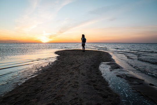 Woman standing on sea coast at sunset