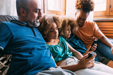 Parents looking at children using smart phones sitting on sofa