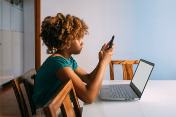 Girl sitting with laptop using smart phone at home