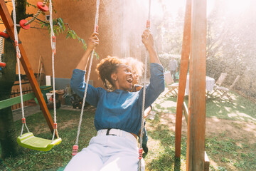 Playful boy pushing mother sitting on swing in backyard