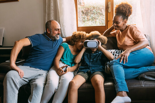 Boy wearing virtual reality simulator sitting by sister and parents on sofa