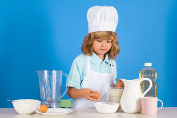 Child chef cook prepares food in isolated blue studio background. Kids cooking. Teen boy with apron and chef hat preparing a healthy vegetables meal in the kitchen.