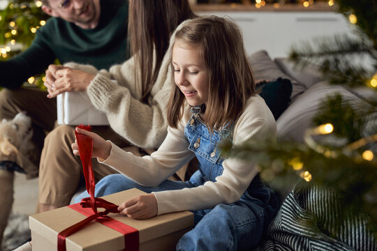 Smiling girl opening Christmas present by parents in living room