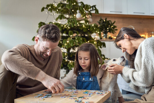 Smiling man and daughter joining puzzle by woman with dog at home