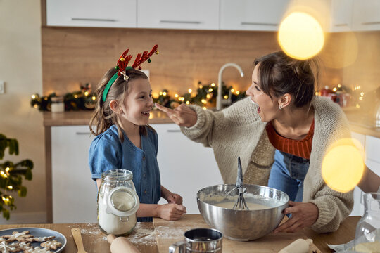 Happy mother putting flour on daughter's nose in kitchen