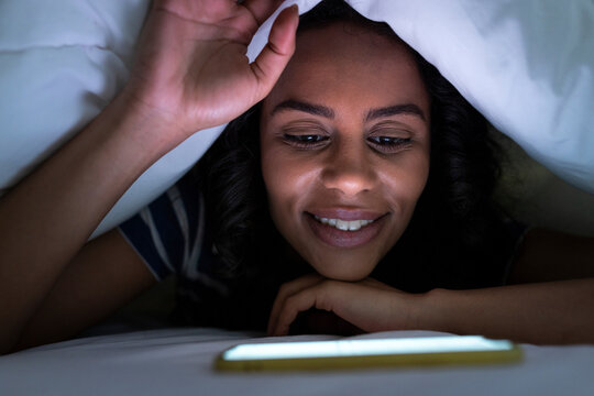 Smiling Woman Watching Movie On Smart Phone Under Blanket At Home