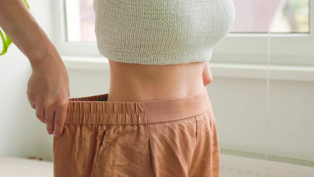 close up of a female slim waist in old jeans after successful diet indoors, weight loss at home. Athletic girl lost weight after diet or exercise