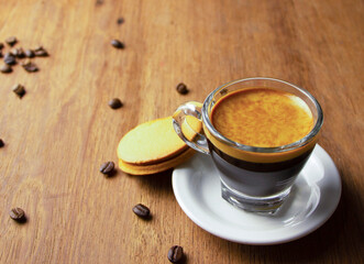 Cup of hot black espresso on wooden background with a piece of pastry , pile of roasted arabica coffee beans.