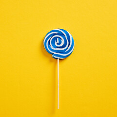 Blue and white colored swirl round candy lollipop on yellow background.