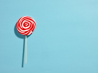 Red and white colored swirl round candy lollipop on blue background. - obrazy, fototapety, plakaty