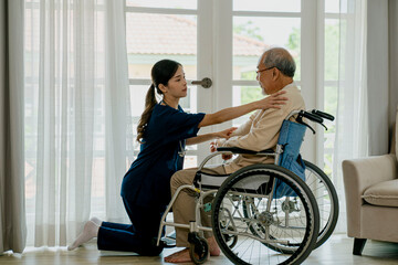 Caring nurse with senior man sitting on wheelchair at home.