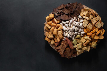 crackers in assortment with different tastes and different shapes and fried salted pistachios are laid out on a wooden substrate. Snacks in assortment on a dark background
