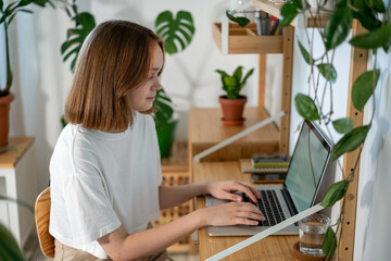 Young woman entrepreneur working on laptop at home. Freelancer typing email on a laptop, girl using a computer for study online at home, female user busy on a distance internet job. Remote online work