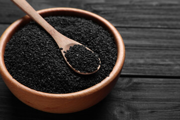 Bowl and spoon with black sesame seeds on wooden table, space for text