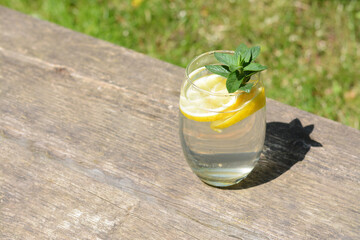 Refreshing water with lemon and mint on wooden table outdoors, space for text