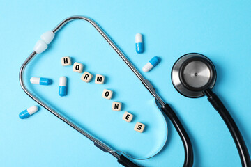 Word Hormones made of wooden cubes with letters, stethoscope and pills on light blue background, flat lay