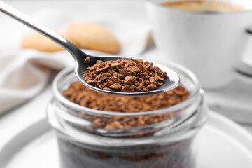 Instant coffee and spoon above glass jar on table, closeup