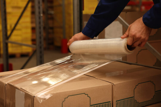 Worker wrapping boxes in stretch film at warehouse, closeup