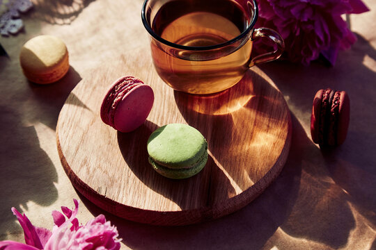 Herbal tea and macarons dessert for brunch. Blooming pink peony flowers under trendy hard shadows. Relaxation, thoughtful, meditative, good mood lifestyle