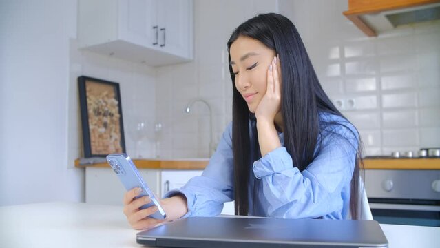 Beautiful Asian girl browsing internet on mobile phone. Pretty young Vietnamese woman using modern blue smartphone for communication. BIPOC person lifestyle video clip