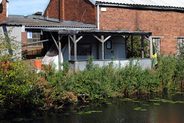 Building with Old Caravan beside Industrial Canal - obrazy, fototapety, plakaty